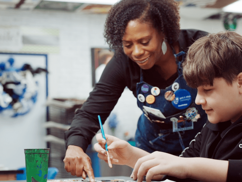A teacher helps a student who is painting.